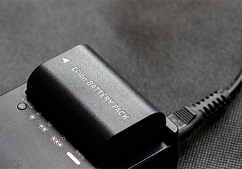A lithium ion battery sits in a power charging cradle with an electric cord.