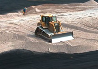 Heavy machinery installing a membrane liner and cap on a closed landfill