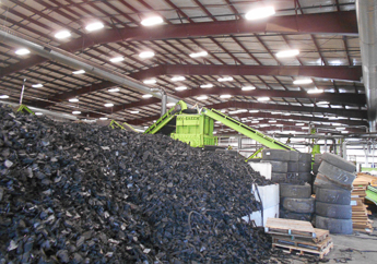 Scrap tire shredder inside a large room with processed tires and stacks of tires located nearby