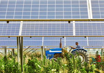 A tractor drives behind a field with a bank of solar panels in the background.