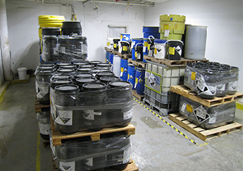 Two rows of stacked drums containing hazardous secondary materials stored in a container storage area