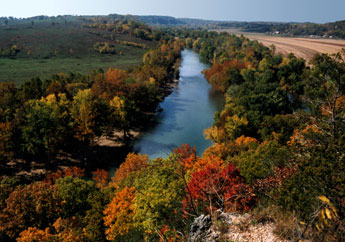 Trees with fall-colored leaves surround the Gasconade River at Portuguese Point in Pulaski County with farmland in the horizon.