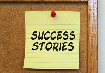 A post-it note that reads "Success Stories", thumb-tacked to a corkboard.