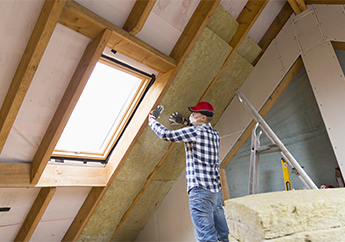 A man installs weatherization around a window in an attic
