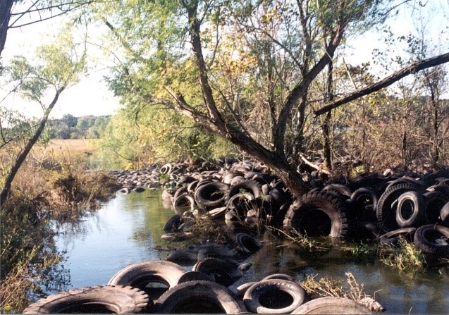 Scrap tires discarded in a stream in a field.