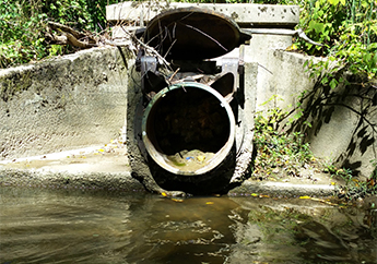 Stormwater flows from a concrete outfall pipe into a stream
