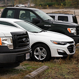 A parked row of cars and trucks in a gravel parking lot