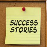 A post-it note that reads "Success Stories", thumb-tacked to a corkboard