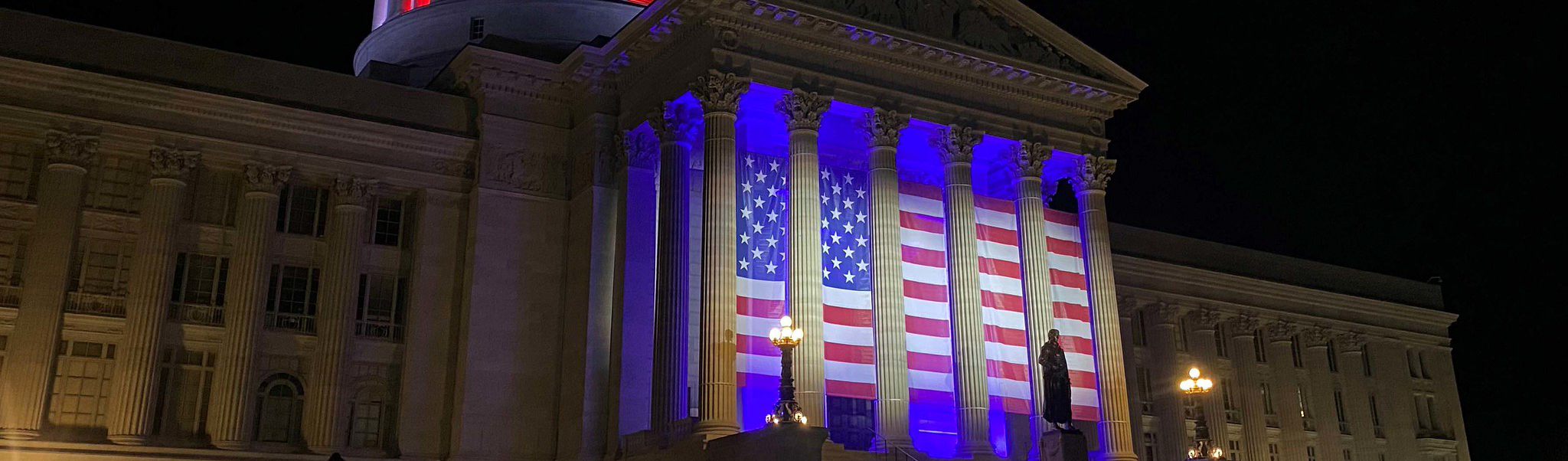 A large American flag is displayed between the 6 pillars to the entrance of the Missouri State Capital in Jefferson City, Missouri