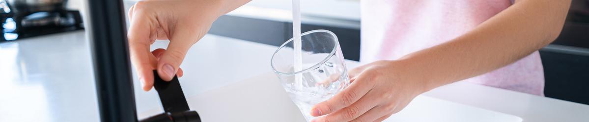 An individual filling a drinking glass with water from a kitchen faucet