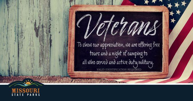 Tours and camping for veterans and active duty military offered as a thank you, shown on a chalkboard with wooden boards and a flag in the background.
