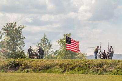 Civil War reenactors stand beside two cannons with an American flag flying between them.