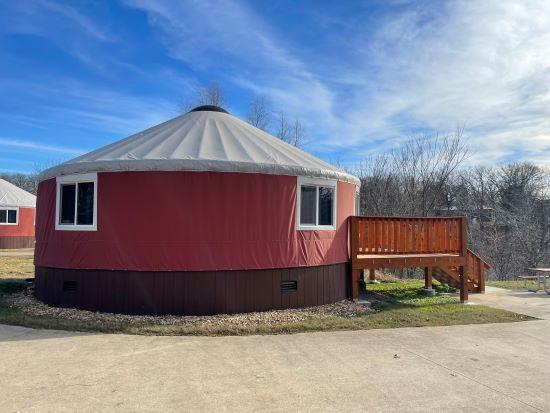 Circular yurt with red sides against a blue sky with leafless trees in background.