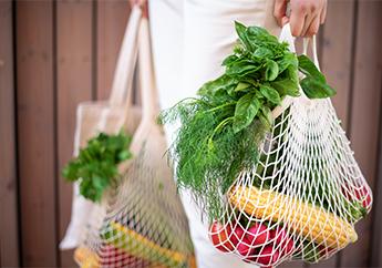 A consumer holding reusable shopping bags full of fresh produce