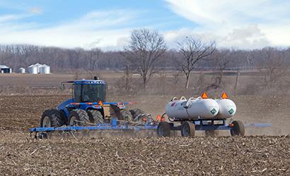 A blue tractor pulling two white anhydrous ammonia tanks fertilizing a field