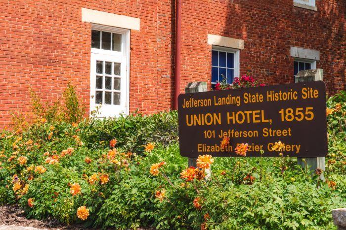Jefferson Landing State Historic Site sign in a garden of flowers in front of the brick building, which is the Union Hotel.