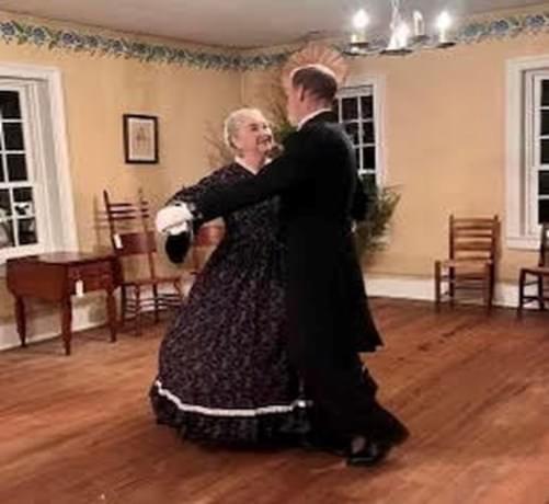 A couple dressed in attire from the late 1800s dance across a ballroom.