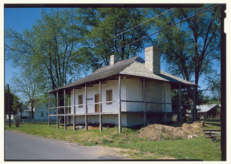 Bequette-Ribault house in Ste. Genevieve with covered porch and mound of dirt at the side. 