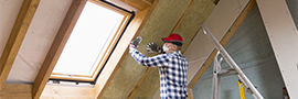 A man installs weatherization around a window in an attic