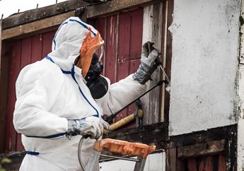 A contractor in a Level B plastic suit and full-face respirator removing asbestos