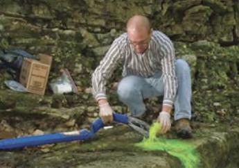 A person conducting water tracing adding nontoxic fluorescent green tracer dye to a creek