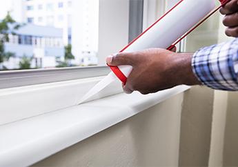 A person uses a caulking gun to apply caulk to a window.