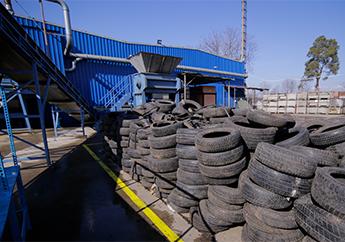 Scrap tire shredder outside a blue building loaded with stacks of tires