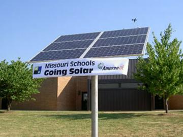 A vinyl Missouri Schools Going Solar banner on a solar grid in front of a school building.
