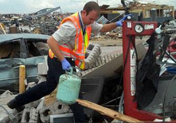 Randall Willoughby picks up a small propane tank amongst the tornado damage including destroyed cars and buildings in Joplin, Missouri.