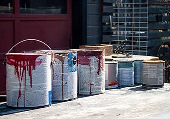 Old paint buckets cans in front of a garage