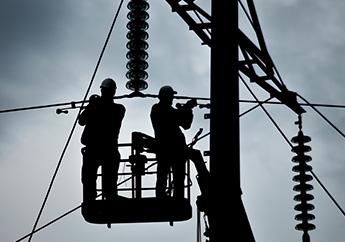 Silhouette of two electric utility lineman in a hydraulic bucket working on high voltage powerlines