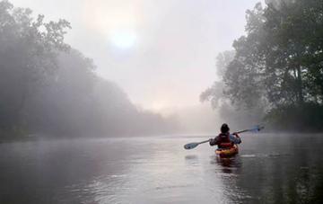 Individual canoeing on the Meramec River through early morning fog