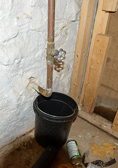 An orange-brown colored copper service line with a black bucket underneath