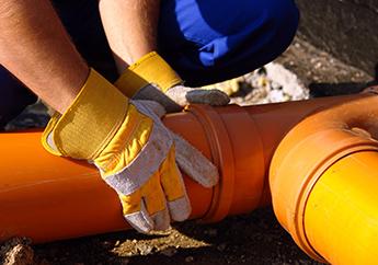 Closeup of plumber's hands assembling orange pvc sewage pipes