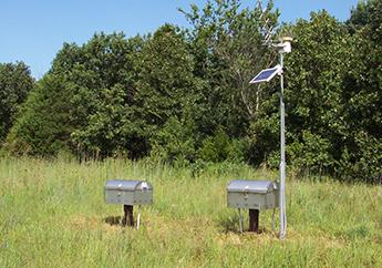 Two water monitoring stations in a grassy field under a blue sky. 
