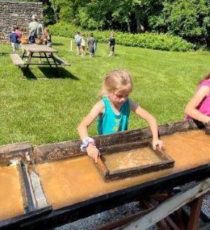 Ralls elementary visits Mark Twain Birthplace as part of bus grant program. Young girl in front uses park equipment to sieve, as other children play on the lawn in the background.