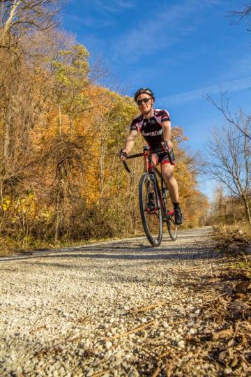 Man riding a bike on a gravel trail with trees flanking him.