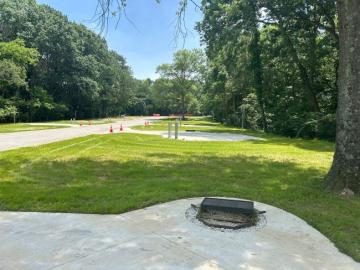 Concrete campground pad with fire pit in foreground. Road in the center of photo leading to other campground pads. 