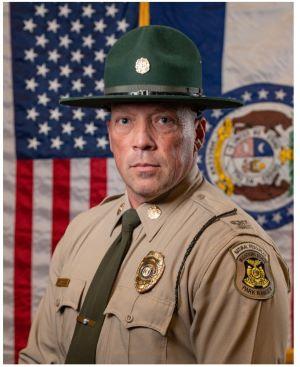 Uniformed State Park Ranger Josh Campbell stands in front of the U.S. and Missouri state flags.