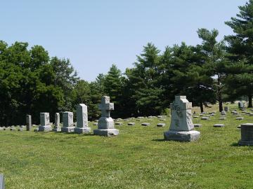 Headstones on green grass and surrounded by trees.