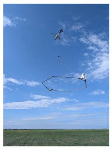 A SkyTEM Helicopter dangling a frame over a field.