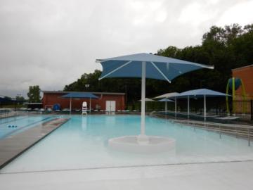shallow pool with blue umbrellas standing tall with a brick building in the back