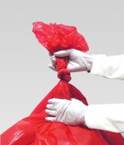 An individual wearing latex gloves closing a red biohazard bag.