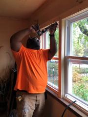 A man installs weatherization caulking around a window sill.